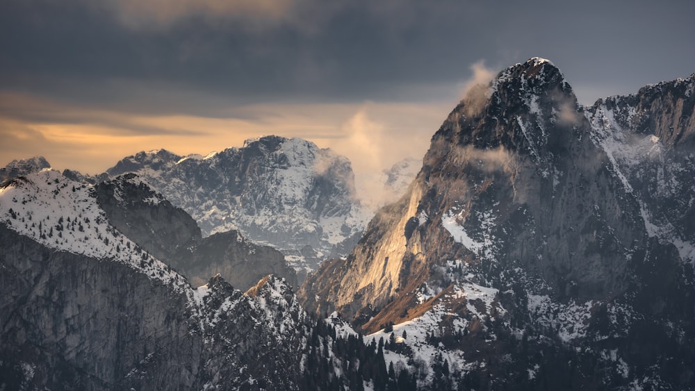 a mountain range covered in snow under a cloudy sky