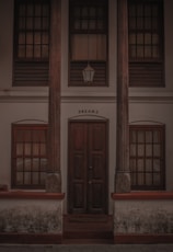 A wooden door is flanked by two tall pillars with intricate carvings. Above the door is a window with wooden shutters and a lantern hanging down. The word 'DREAMZ' is inscribed above the door. The building has a weathered look, with visible signs of age and wear.