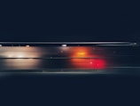A dynamic image featuring motion blur with vibrant streaks of red and orange against a dark background, possibly indicating light trails seen through a window at night.