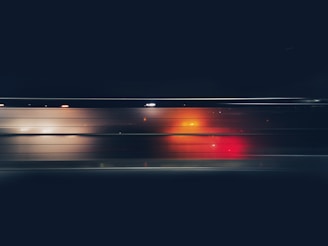 A dynamic image featuring motion blur with vibrant streaks of red and orange against a dark background, possibly indicating light trails seen through a window at night.
