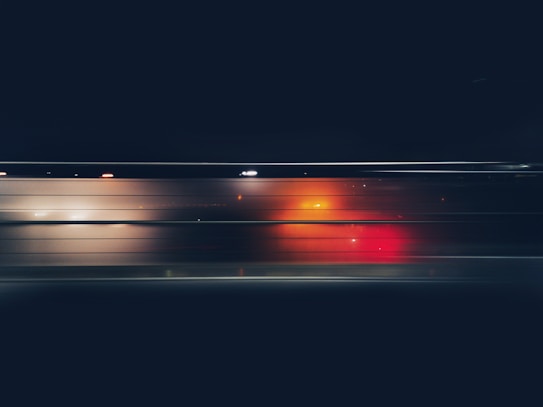 A dynamic image featuring motion blur with vibrant streaks of red and orange against a dark background, possibly indicating light trails seen through a window at night.