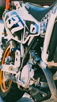 A close-up view of a dirt bike focusing on its mechanical parts and decals. The number 37 is prominently displayed on the side, with visible branding and details of the bike's engine and framework.