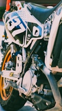 Close-up of João Gabriel's motocross bike with sponsor logos and dirt background.