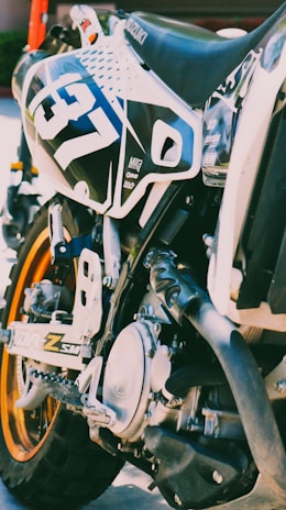 Close-up of João Gabriel's motocross bike with sponsor logos and dirt background.