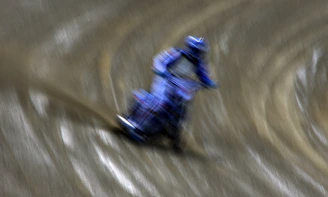 Dynamic image of a motorcycle speeding through a dirt track kicking up dust, captured with motion blur.