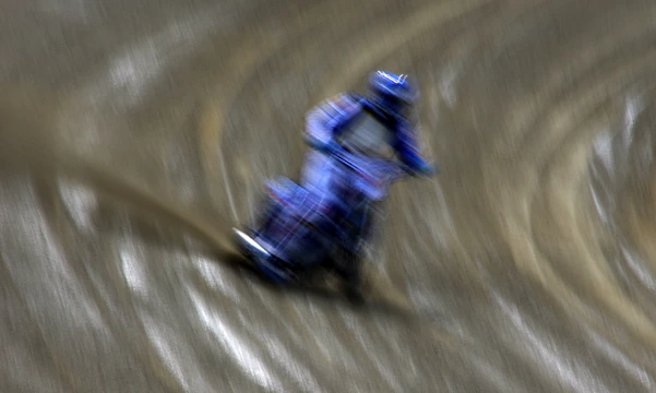 Dynamic image of a motorcycle speeding through a dirt track kicking up dust, captured with motion blur.
