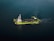 A green and white ship is sailing through calm, dark blue waters. The vessel appears to be equipped with various industrial machinery on its deck, indicating it might be a workboat or a dredger.