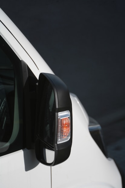 A close-up view of a vehicle's side mirror, featuring an integrated indicator light with a black casing. The white body of the vehicle contrasts against the dark background.