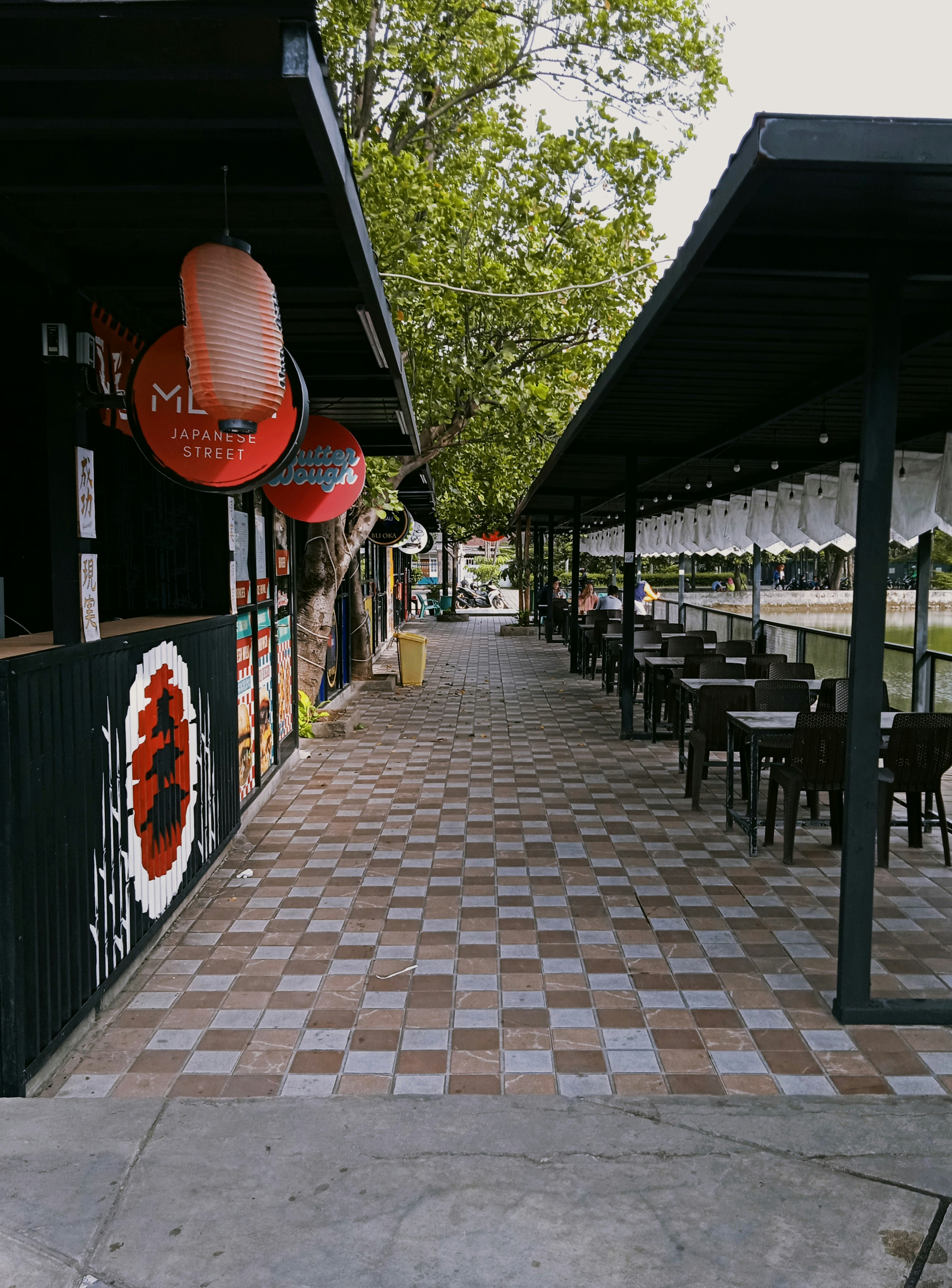 a sidewalk lined with tables and chairs under umbrellas