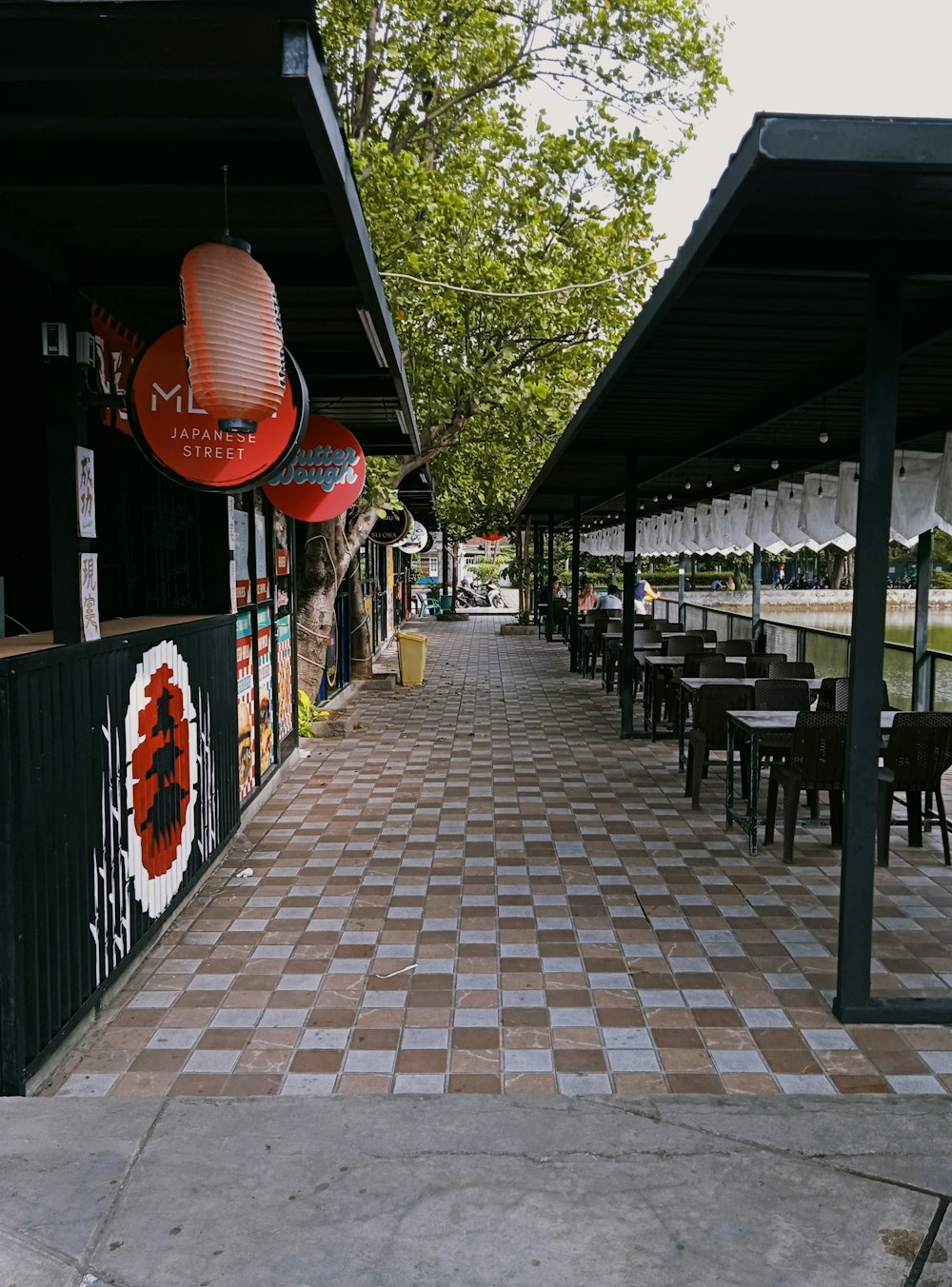 a sidewalk lined with tables and chairs under umbrellas