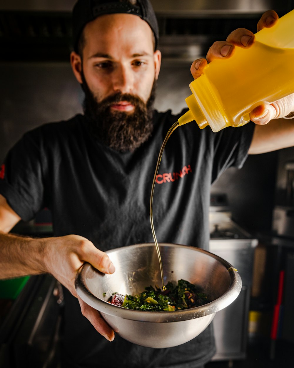 a man pouring mustard into a bowl of greens