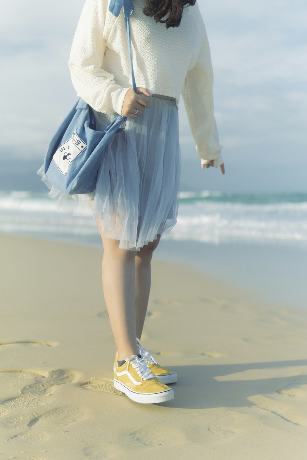 a woman standing on a beach holding a blue purse