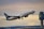 A commercial airplane is taking off, with its nose pointed upward. The aircraft is painted in the colors and logo of WestJet. In the background, there is an airport control tower and a sky filled with clouds displaying various hues, suggesting either dawn or dusk.