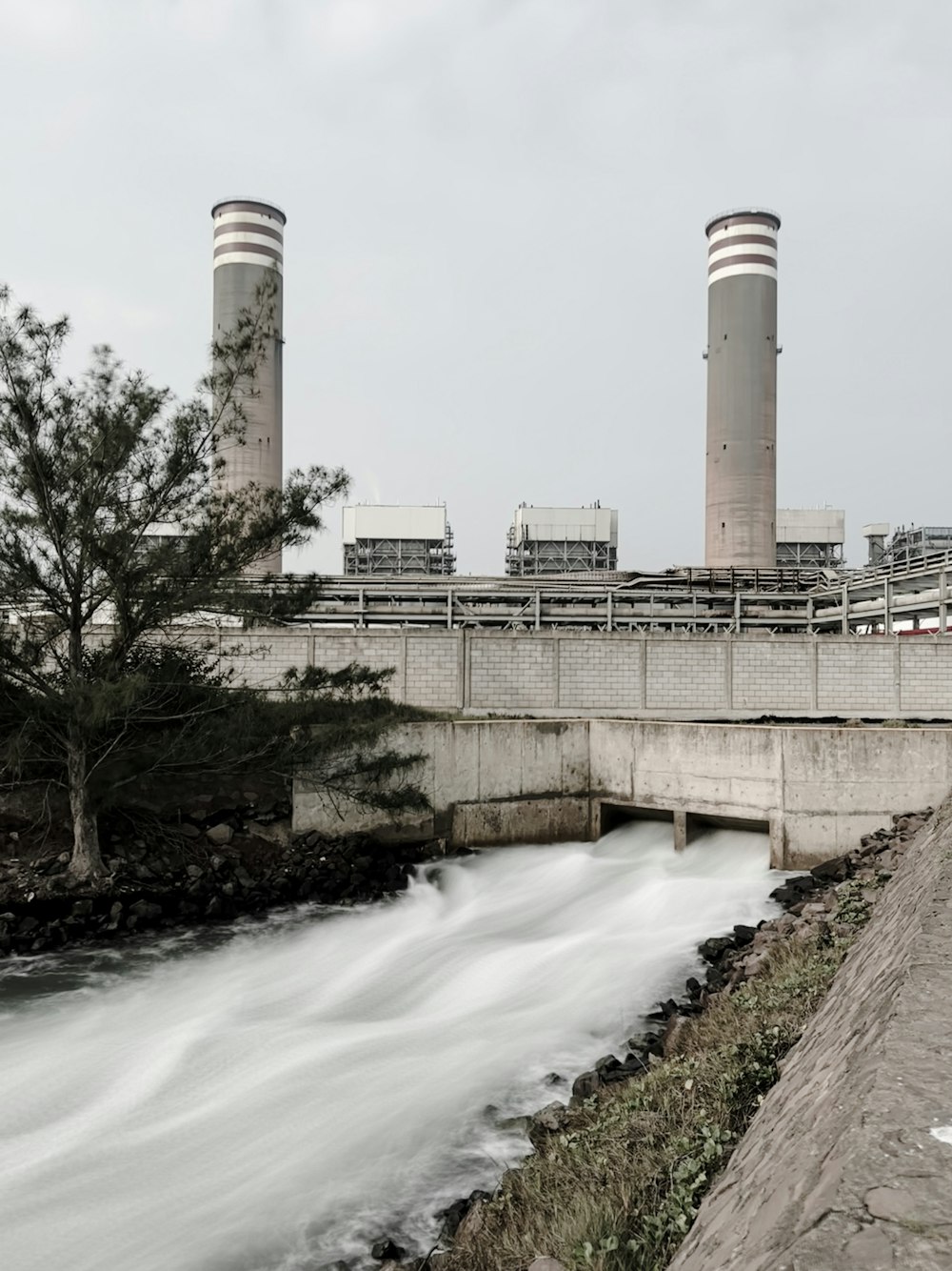 a river running under a bridge next to a power plant