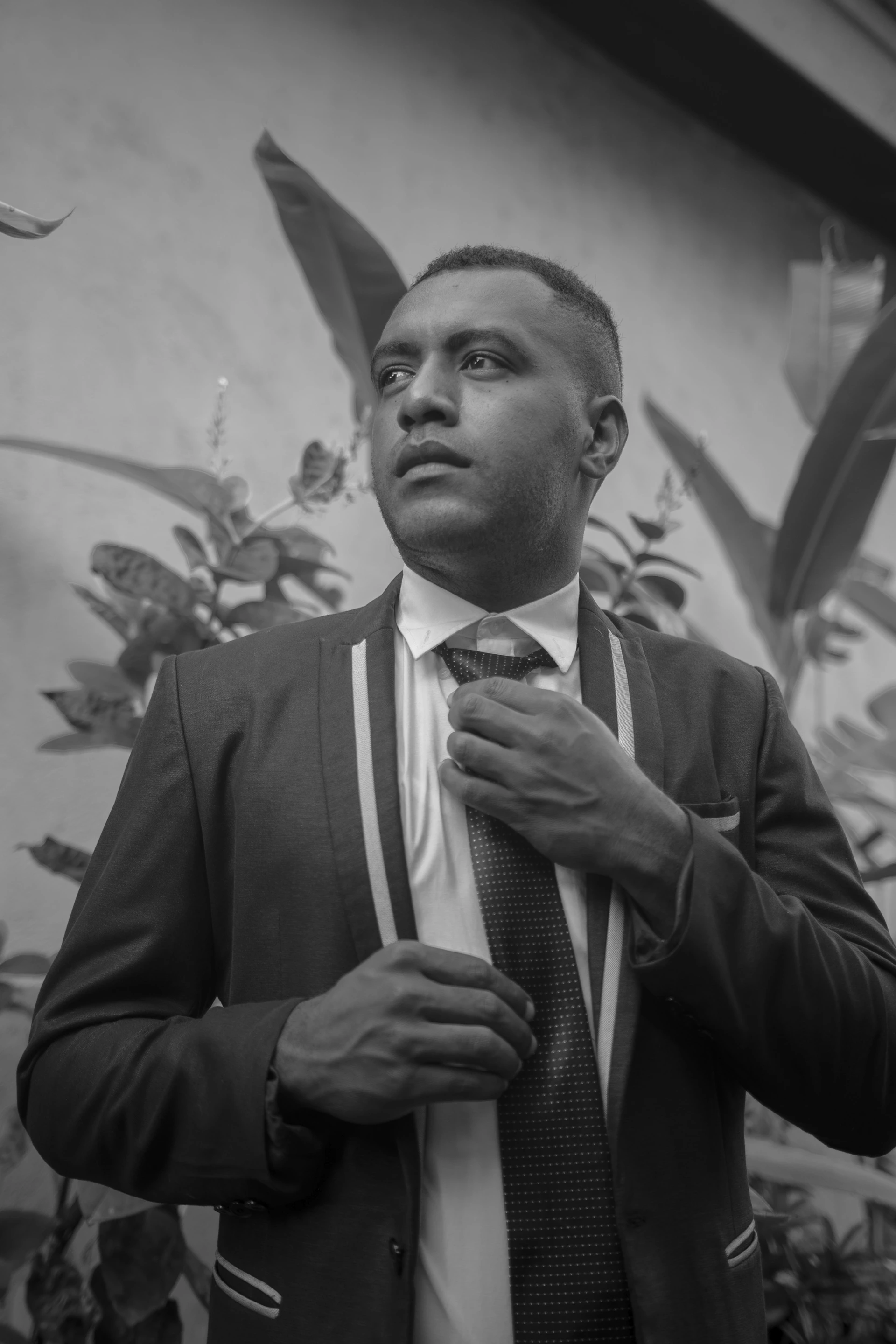 The groom adjusting his tie with a focused expression, framed by elegant black and white tones.