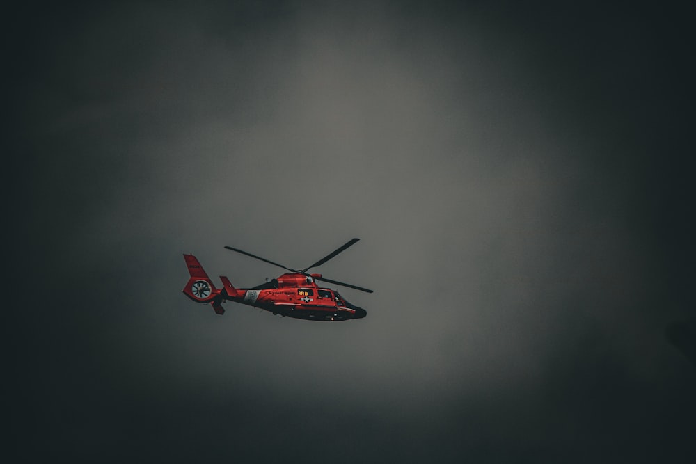 a red helicopter flying through a cloudy sky