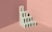A minimalist, abstract sculpture resembling a series of interconnected arches is placed in a corner with pink walls and floor. The structure is bathed in soft lighting, creating shadows that add depth and dimension to the scene.