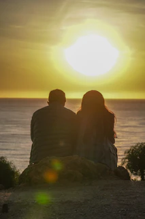 A serene image of a couple sitting close on a soft sand hill, bathed in warm late afternoon light.