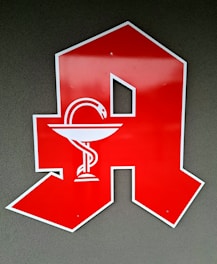 A large red letter 'A' is displayed against a gray background. Inside the letter is a white emblem of a snake wrapped around a bowl, commonly associated with pharmacy or apothecary symbols.