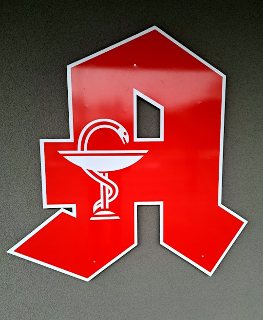 A large red letter 'A' is displayed against a gray background. Inside the letter is a white emblem of a snake wrapped around a bowl, commonly associated with pharmacy or apothecary symbols.