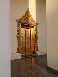 Luxury steel door with intricate patterns and gold trim, set against a minimalist villa facade with lush greenery