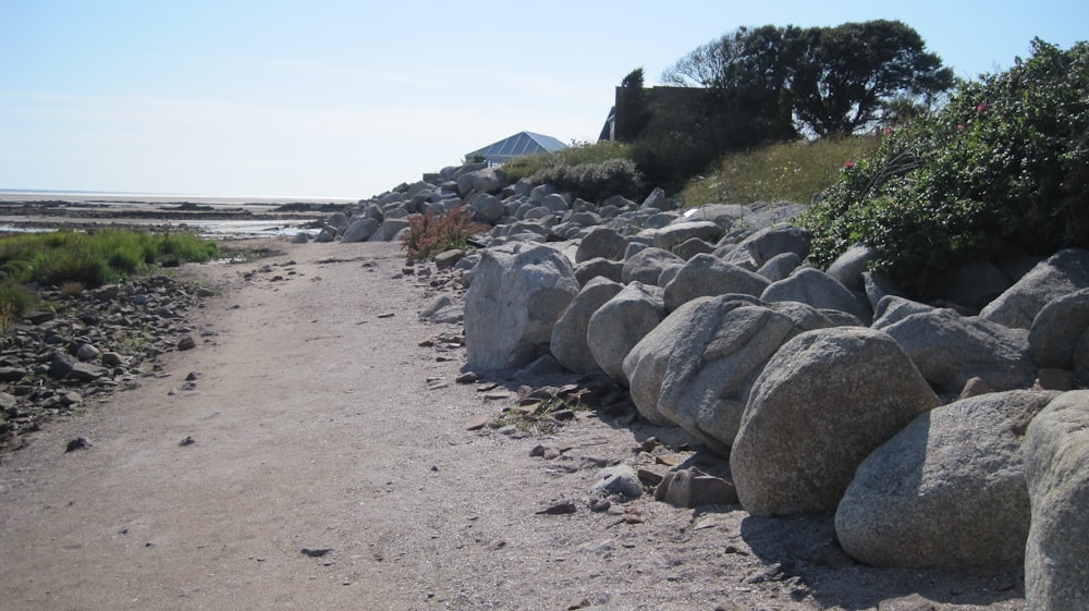 Un camino de tierra bordeado de grandes rocas junto a un cuerpo de agua