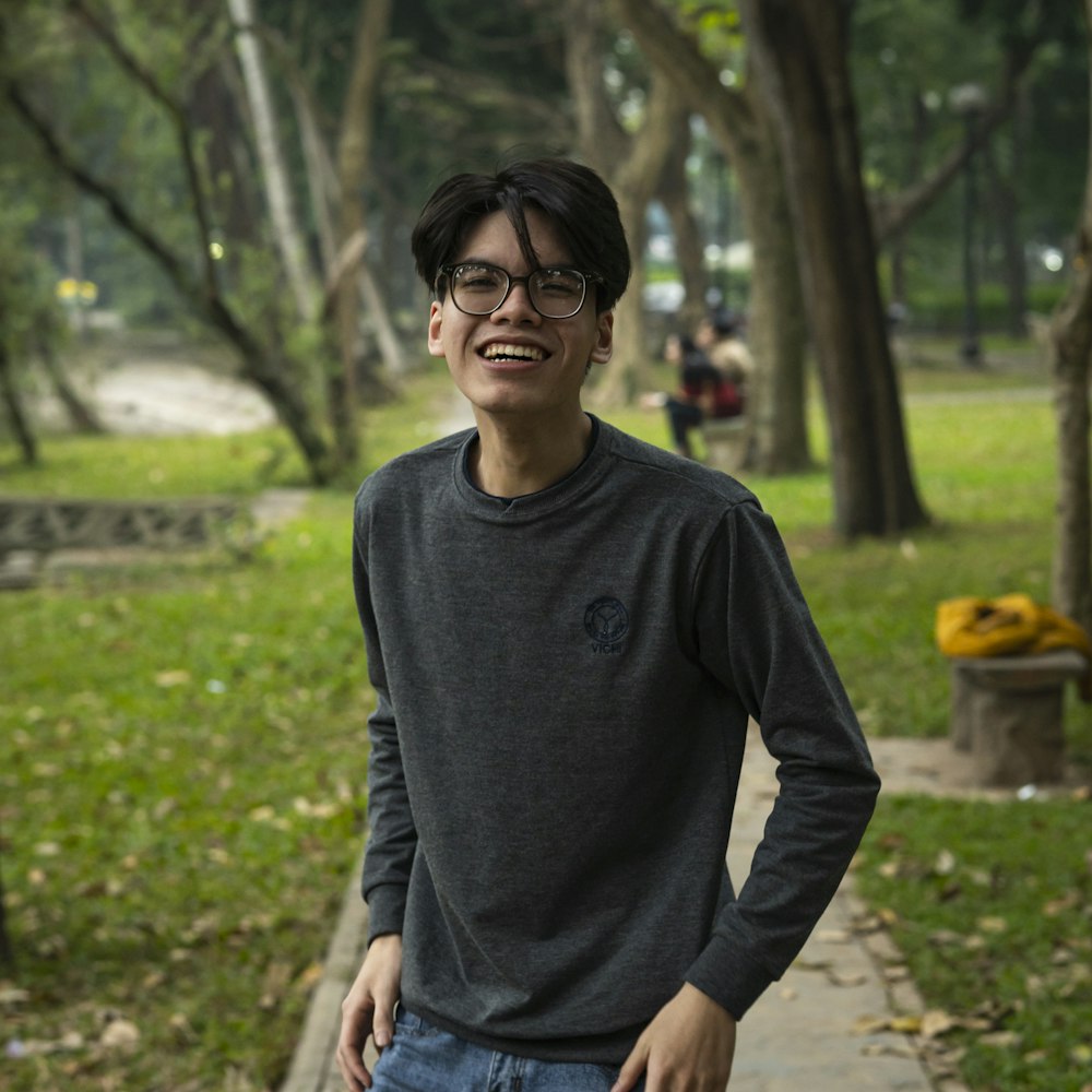 a young man standing in a park with trees in the background