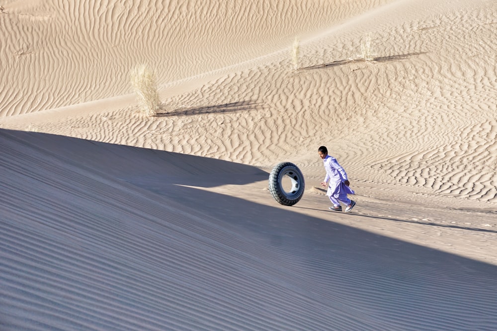 a man walking across a sandy field next to a tire