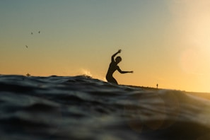 A surfer gliding effortlessly on a Surf IQ electric surfboard over crystal-clear blue waves at sunset.