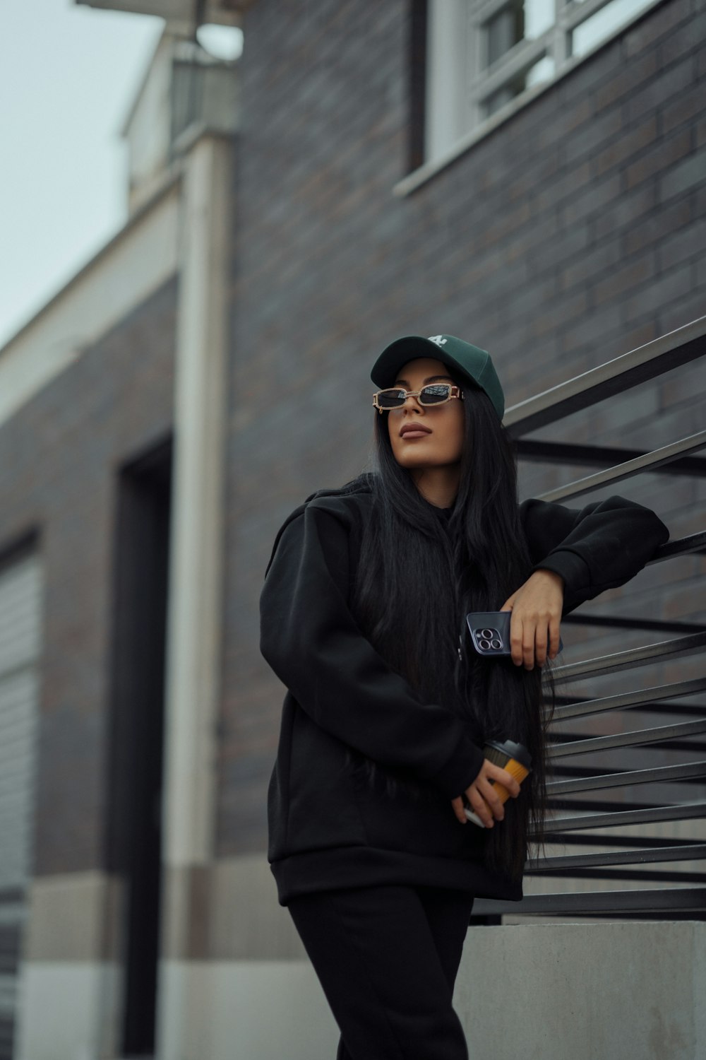 a woman wearing a hat and sunglasses standing next to a building