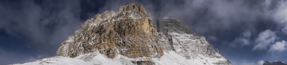 a very tall mountain covered in snow under a cloudy sky