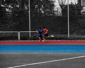 Athlete sprinting on an outdoor track with a coach observing and timing the run.