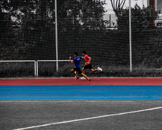 Athlete sprinting on an outdoor track with a coach observing and timing the run.