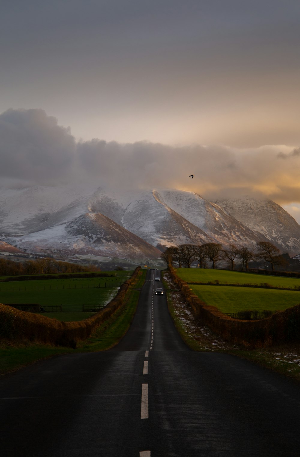 a long road with snow covered mountains in the background