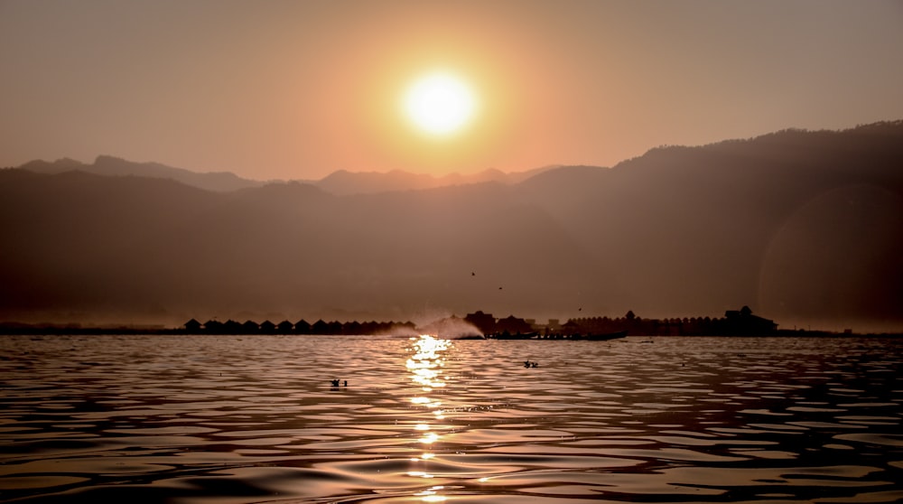 the sun is setting over a lake with mountains in the background