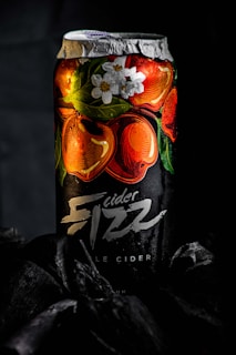 A can of cider with a predominantly black label featuring vibrant illustrations of red apples and white flowers. The brand name 'Fizz' is prominently displayed in a bold, stylized font. The can is set against a dark background, enhancing the vividness of the design.