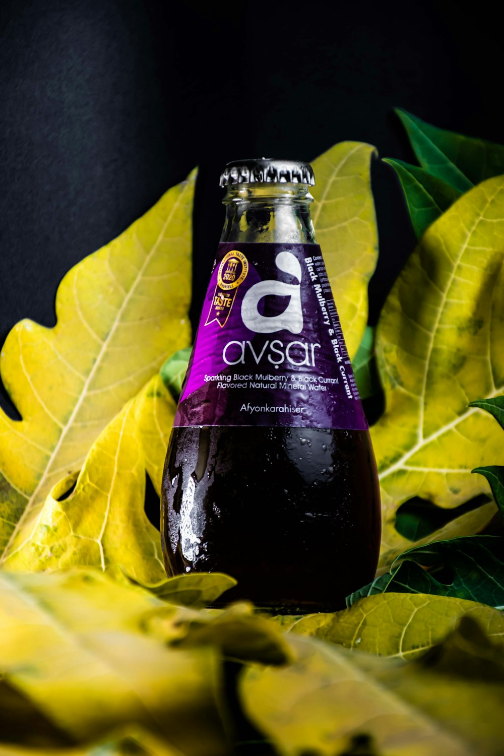 a bottle of purple liquid sitting on top of green leaves