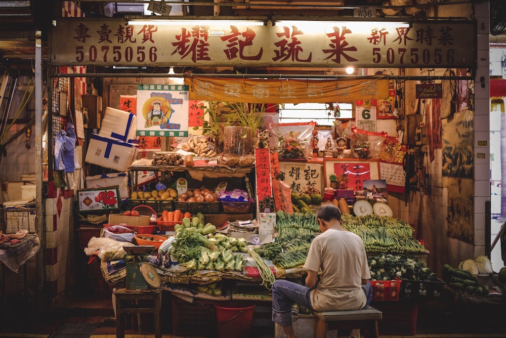 a man sitting on a bench in front of a fruit and vegetable stand