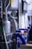 A cluttered industrial or mechanical workspace with various machines and equipment. There is a complex apparatus with pipes and metallic components, alongside a desk holding cleaning supplies, sprays, and folders. A digital screen is mounted on the wall, possibly for monitoring or control purposes.
