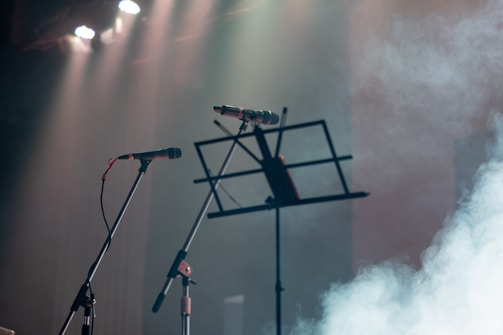 Four glowing microphone stands lined up on a stage with colorful spotlights.