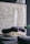 A cozy, textured blanket is artfully arranged on a dark surface, with a modern wall art piece featuring black specks in the background. A large, transparent glass orb hangs above, adding a reflective quality and contemporary feel to the space.