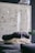 A cozy, textured blanket is artfully arranged on a dark surface, with a modern wall art piece featuring black specks in the background. A large, transparent glass orb hangs above, adding a reflective quality and contemporary feel to the space.