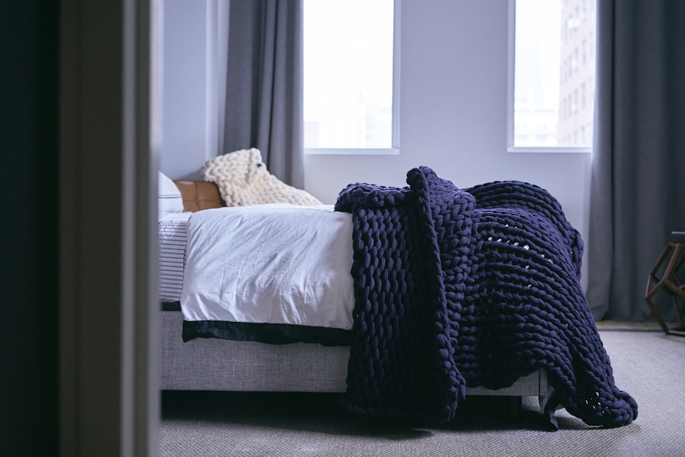 a bed with a blanket on top of it next to a window