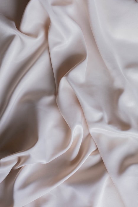 Smooth and flowing white fabric with gentle, soft folds creating an elegant and luxurious texture.