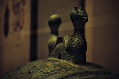 A close-up photograph of a delicate bronze antique sculpture with intricate details and patina.