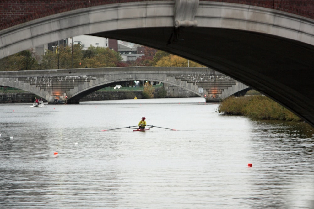 a person rowing a boat under a bridge