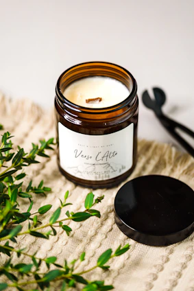 A modern scented candle with a sleek black container, surrounded by fresh flowers.