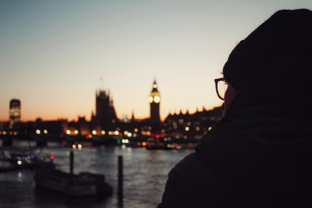 a person standing in front of a body of water with a clock tower in the