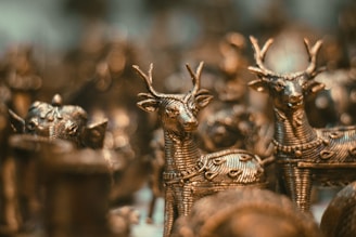 Intricately designed metal figurines of deer are closely arranged, showcasing detailed craftsmanship with textured patterns on their bodies. The focus is on the elegant forms and antlers of the deer, with a soft bokeh effect creating a warm ambiance in the background.