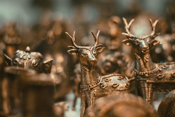 Intricately designed metal figurines of deer are closely arranged, showcasing detailed craftsmanship with textured patterns on their bodies. The focus is on the elegant forms and antlers of the deer, with a soft bokeh effect creating a warm ambiance in the background.